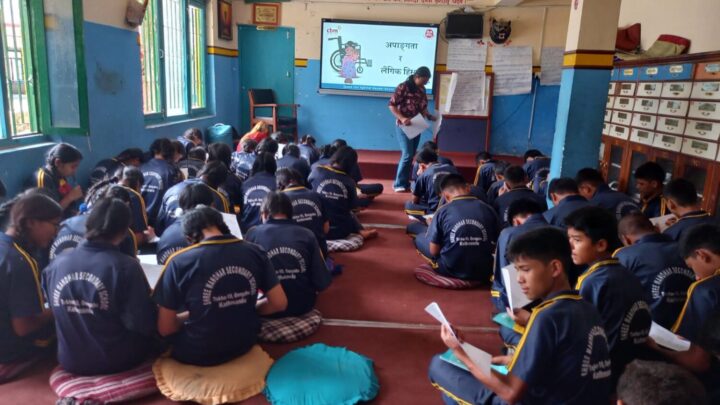 The participants are in the school hall sitting on cushions on the floor. They are facing towards the screen with their back at the camers. The participants are filling the pre-test questionnaire. The screen reads GBV and disability.