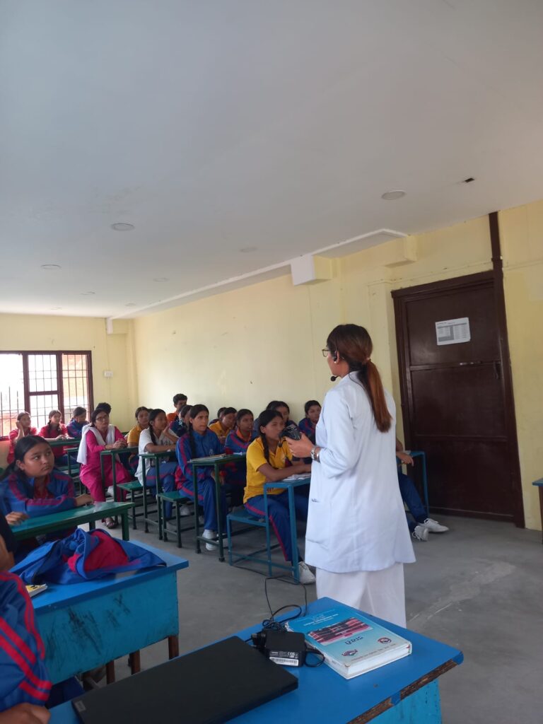The school nurse has her white coat on and she is giving a session on disability and GBV. The students are sitting on the bench and seem keen towards the session.