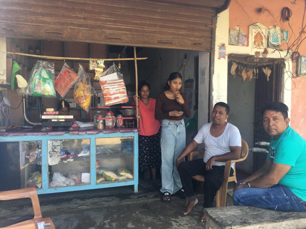 This is a photo of store that Min Bahadur. There are two young girls standing in front of the store. One man is sitting beside Mon Bahadur.