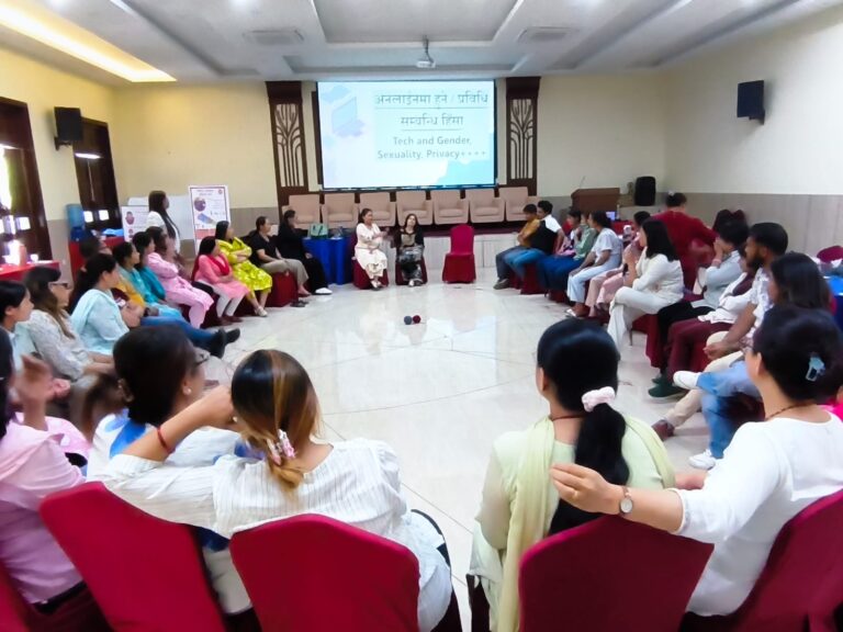 The participants are sitting in a round shape in chairs. There is a net of different colored wools. The participants are sharing their experiences.